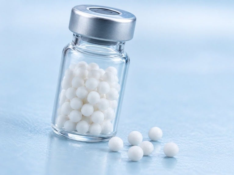Glass vial filled with white lyophilized reagent beads, about 3 mm in diameter, with a few beads on the bench